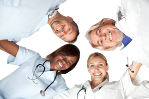 Four Medical Professionals standing in a circle and looking down at the camera on the floor while smiling. 